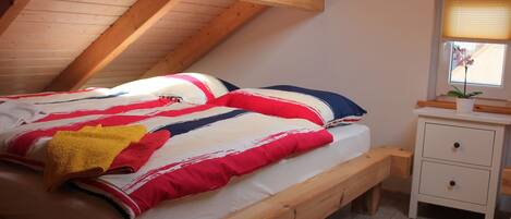 Un dormitorio tipo loft con una cama de madera, una mesita de noche pequeña y una ventana con persianas.