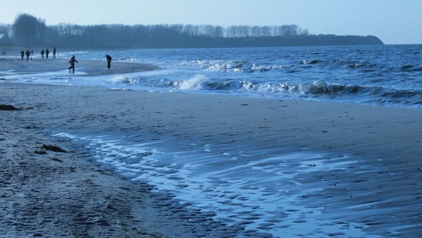 Ein Strand mit Menschen, die am Ufer entlanggehen.