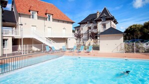 Ein Schwimmbecken mit Liegestühlen, einer Treppe und einem Gebäude mit rotem Dach.