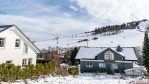 Ein Wohngebiet mit Häusern, einer Skipiste und einer Seilbahn im Hintergrund.