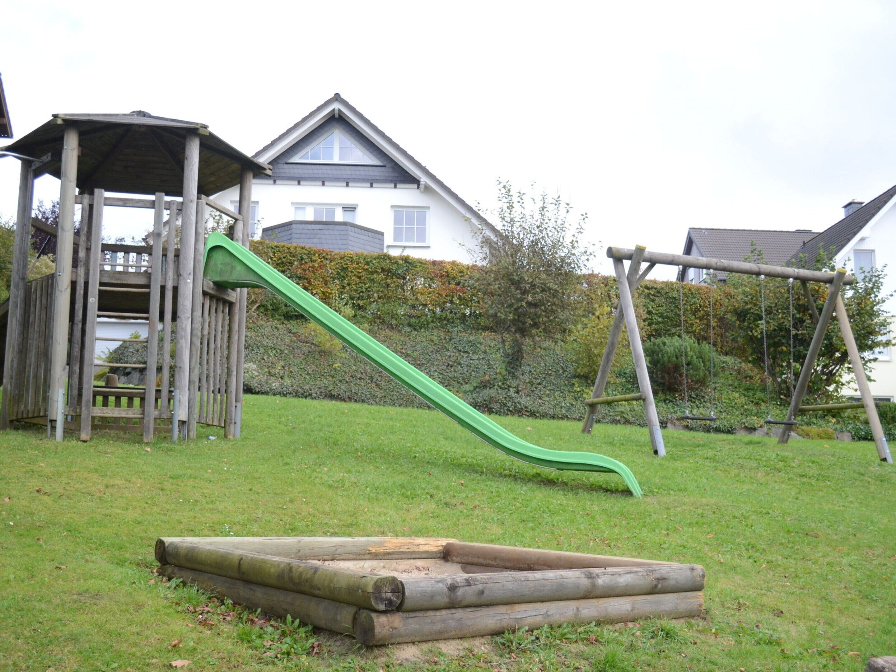 Une aire de jeux avec un toboggan, des balançoires et une structure de jeu en bois.
