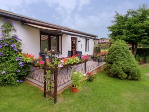 A white house with a balcony, surrounded by a well-maintained garden with various plants and flowers. - Gartenwohnung in Hasselfelde (Oberharz am Brocken)