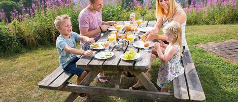 A family dining outdoors at a wooden picnic table with a scenic view in the background.