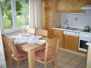 Une cuisine avec des meubles en bois, une table à manger dressée pour quatre personnes et une fenêtre donnant sur un paysage verdoyant.