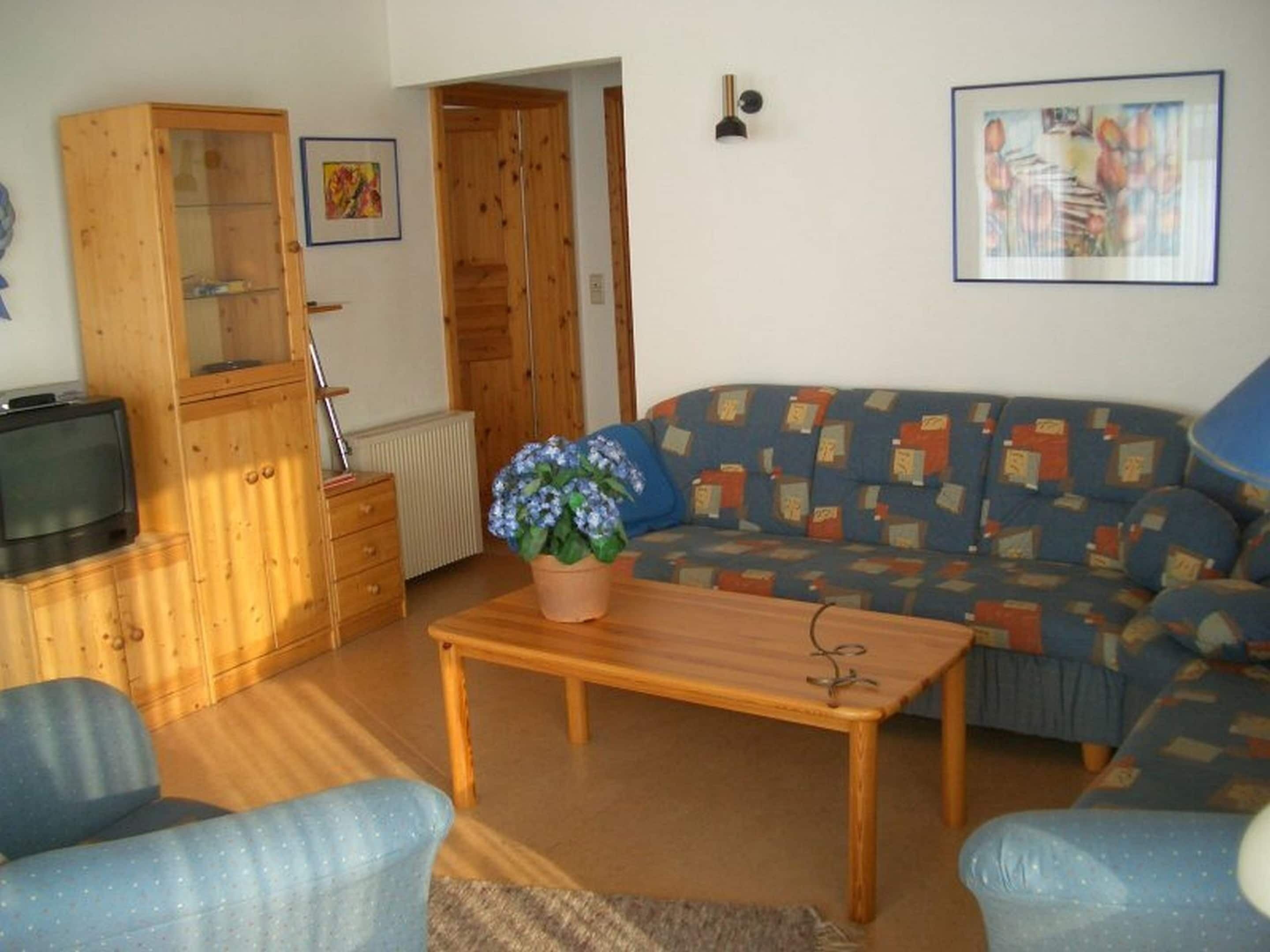 Een woonkamer met een bank, een houten kast, een televisie en een plant in pot.