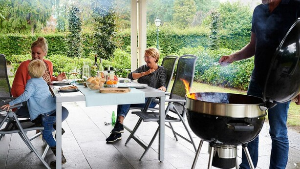 Un espace extérieur aménagé pour les repas, avec un patio couvert, une table dressée et une personne qui fait griller de la nourriture.