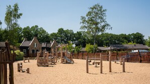 Un espace de jeux sablonneux avec des structures en bois et un bâtiment en briques en arrière-plan.