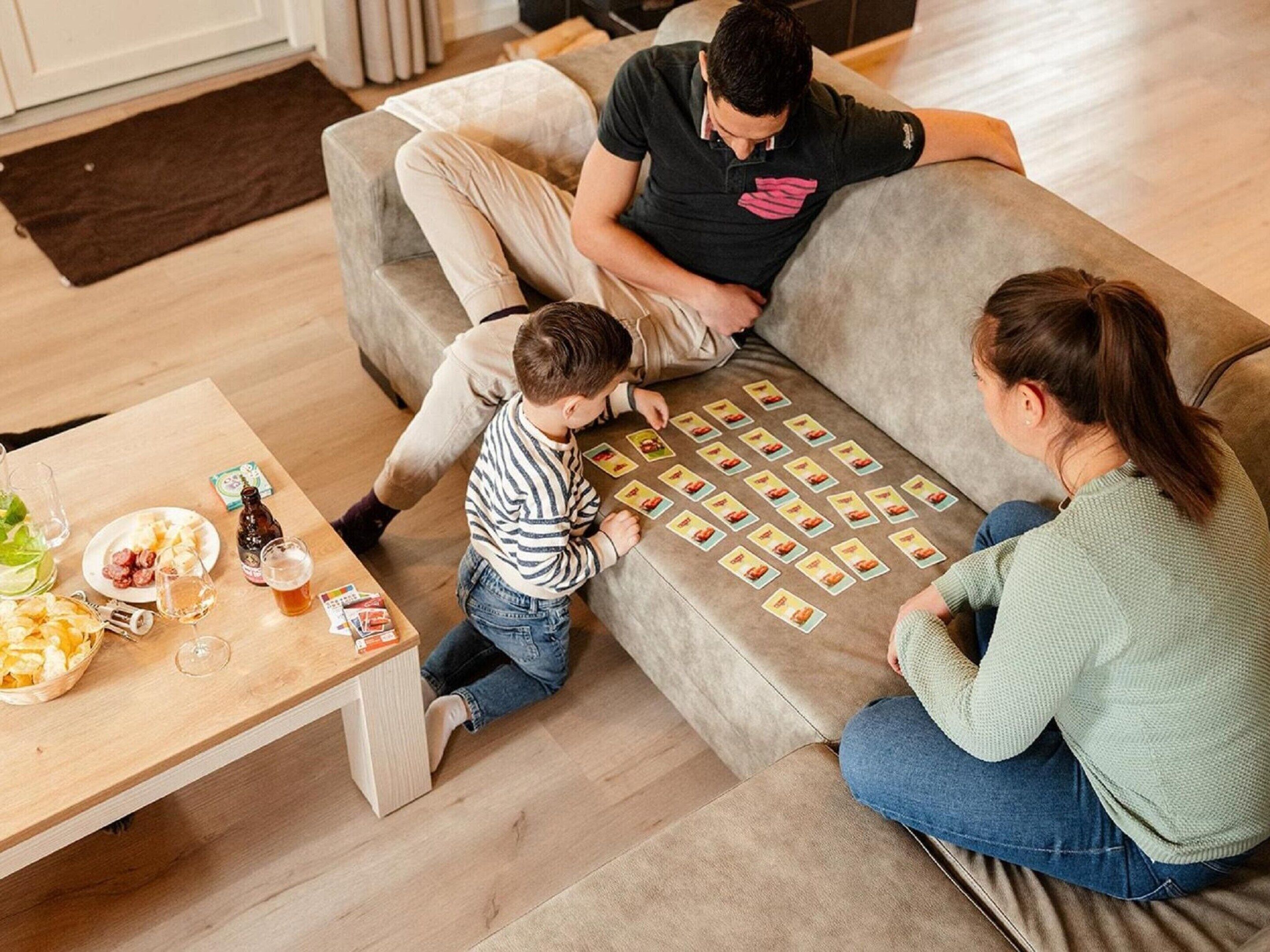 A family playing a card game on a couch with snacks and drinks on a table.