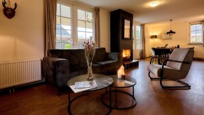 Un salon chaleureux avec une cheminée, un canapé, une table basse et un coin repas comprenant une chaise et une table.