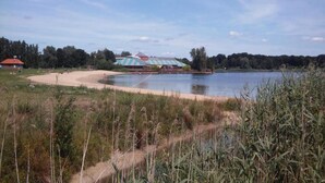 Une zone au bord d’un lac, avec un bâtiment doté d’un toit à rayures, entouré d’arbres et bordé d’une plage de sable.