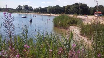 Een meer met bootjes, een zandstrand en omliggende begroeiing.