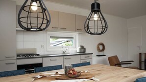 Una cocina moderna con armarios blancos, una mesa de comedor de madera y dos lámparas colgantes negras.