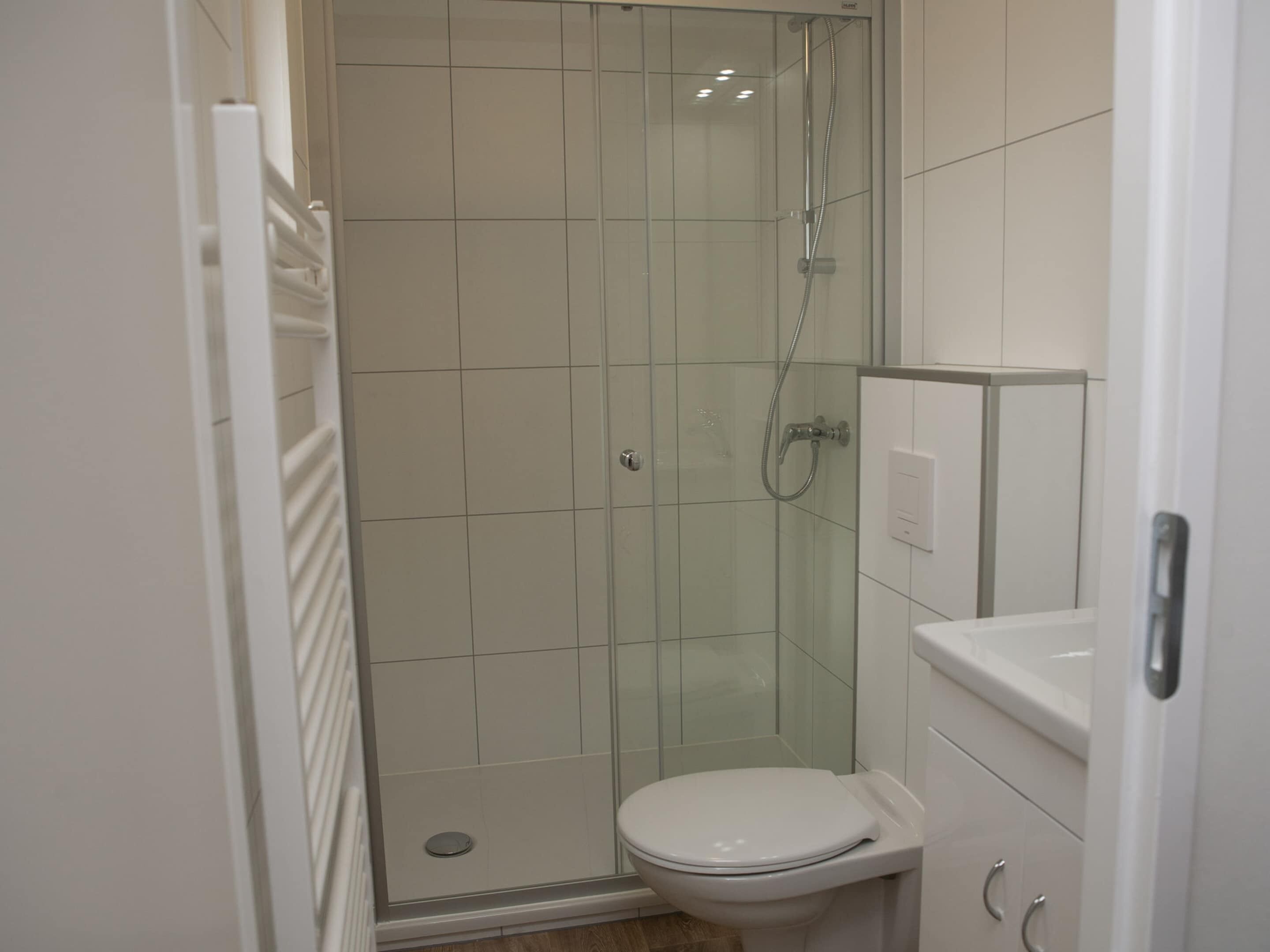 Ett litet, modernt badrum med en dusch som är avskärmad med glasväggar, en vit toalett och ett vitt handfat.