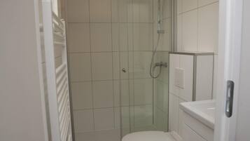 Ett litet, modernt badrum med en dusch som är avskärmad med glasväggar, en vit toalett och ett vitt handfat.
