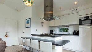 A modern kitchen with a central island, white cabinetry, and stainless steel appliances. - Charming Chalet With Dishwasher in Noordwijk (Noordwijk)