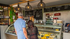 A café with a glass display case filled with desserts, a chalkboard menu, and hanging pendant lights. - Charming Chalet With Dishwasher in Noordwijk (Noordwijk)