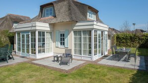 A house with a thatched roof, large windows, and a patio with outdoor furniture. - Restyled Thatched Villa Near the Sea in Cosy Domburg (Domburg)