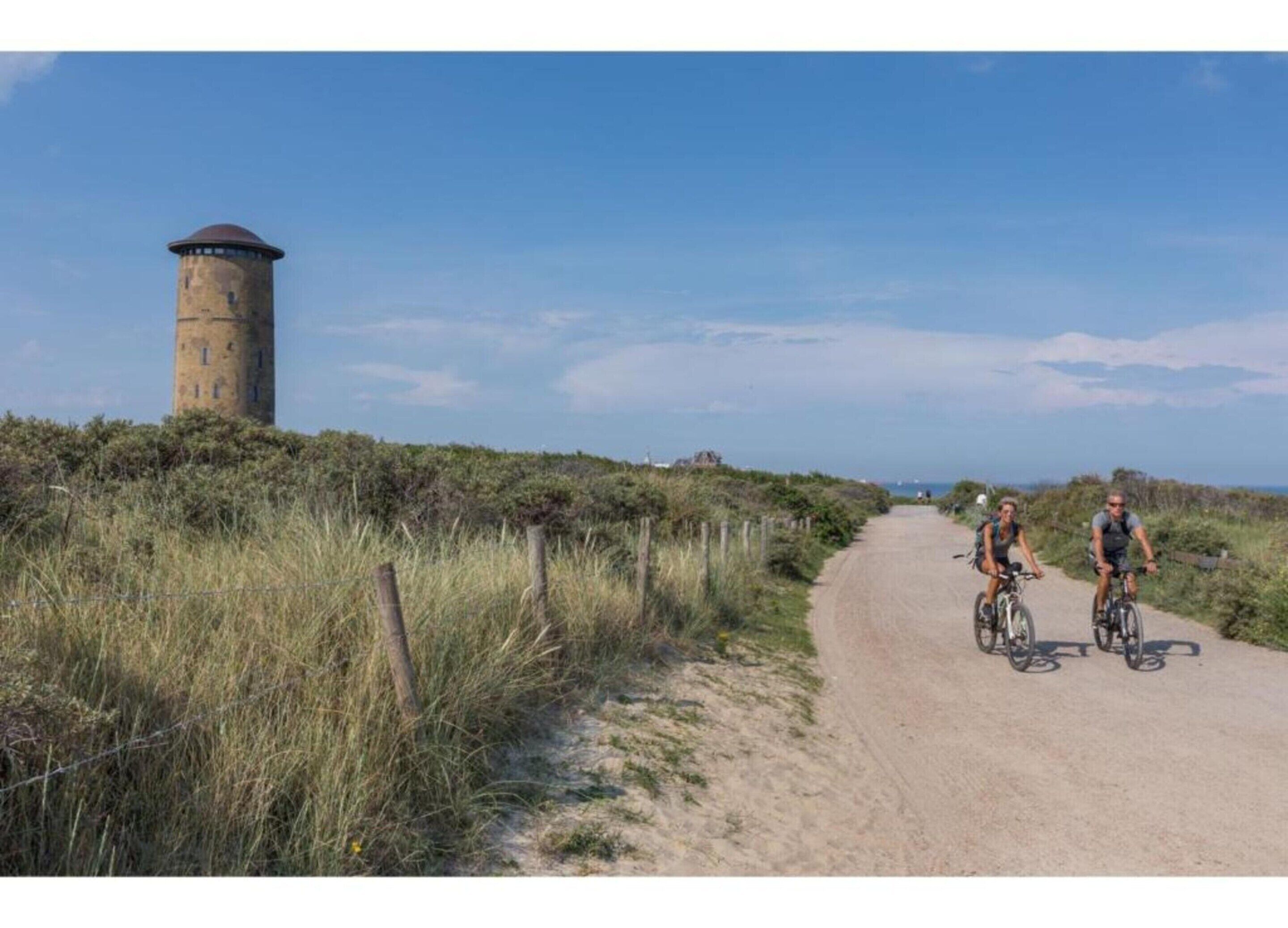 Un sendero de tierra con dos ciclistas, una torre y una valla.