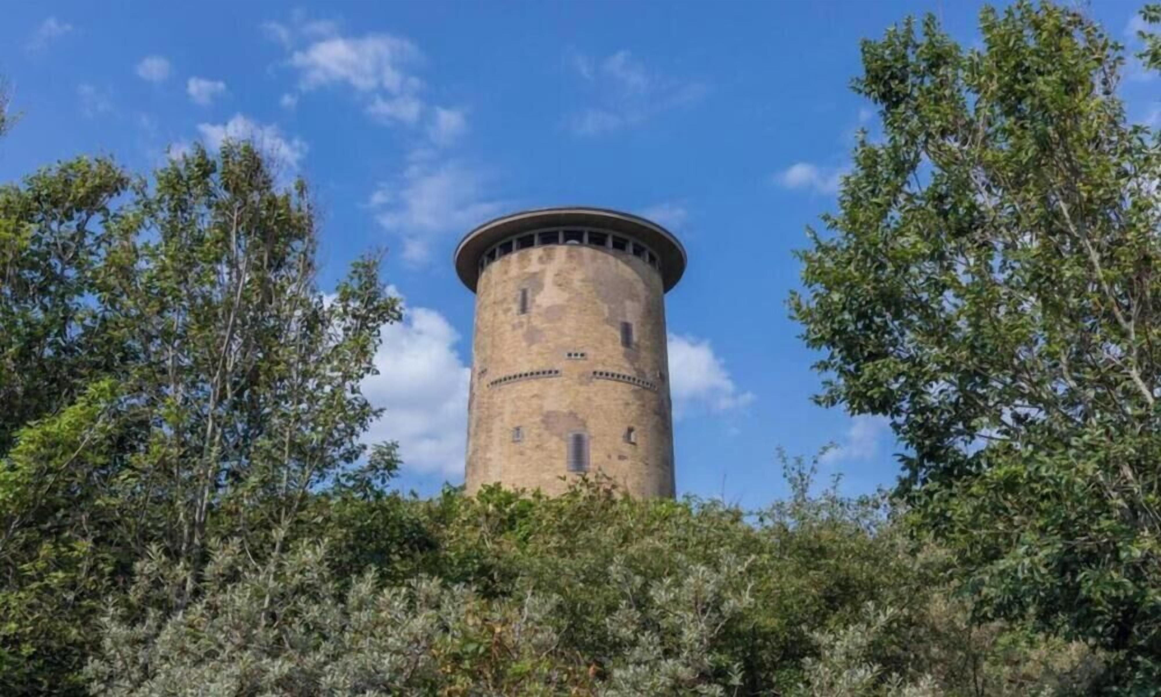 A cylindrical tower with a flat top, surrounded by dense foliage.