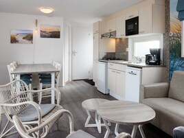 A compact kitchen with a microwave, stove, and coffee maker, adjacent to a dining area with wicker chairs and a small table.