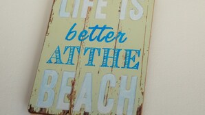 Een verweerd bord met de tekst 'LIFE IS better at the beach'.