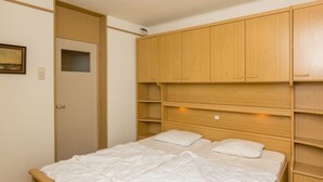 Een slaapkamer met een houten bedframe, een wit matras en een houten garderobe met verschillende planken.