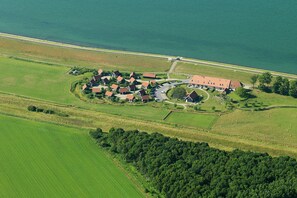 Eine Vogelperspektive auf ein Küstendorf, dessen Häuser in einem Kreis um ein zentrales Gebäude, vermutlich ein Gemeinschaftshaus oder eine Kirche, angeordnet sind, mit einer Straße, die dorthin führt.