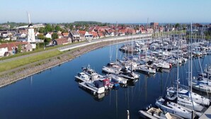Een jachthaven met veel boten afgemeerd langs een smalle waterweg, omringd door huizen en een windmolen.
