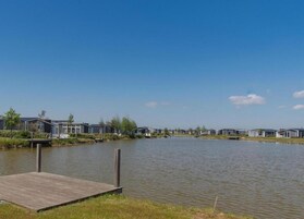 Una hilera de cabañas modernas de un solo piso con un muelle que se adentra en un lago tranquilo, rodeado de vegetación.