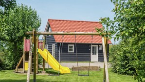 Een speeltuin met een gele glijbaan en schommels, met op de achtergrond een huis met een rood dak.