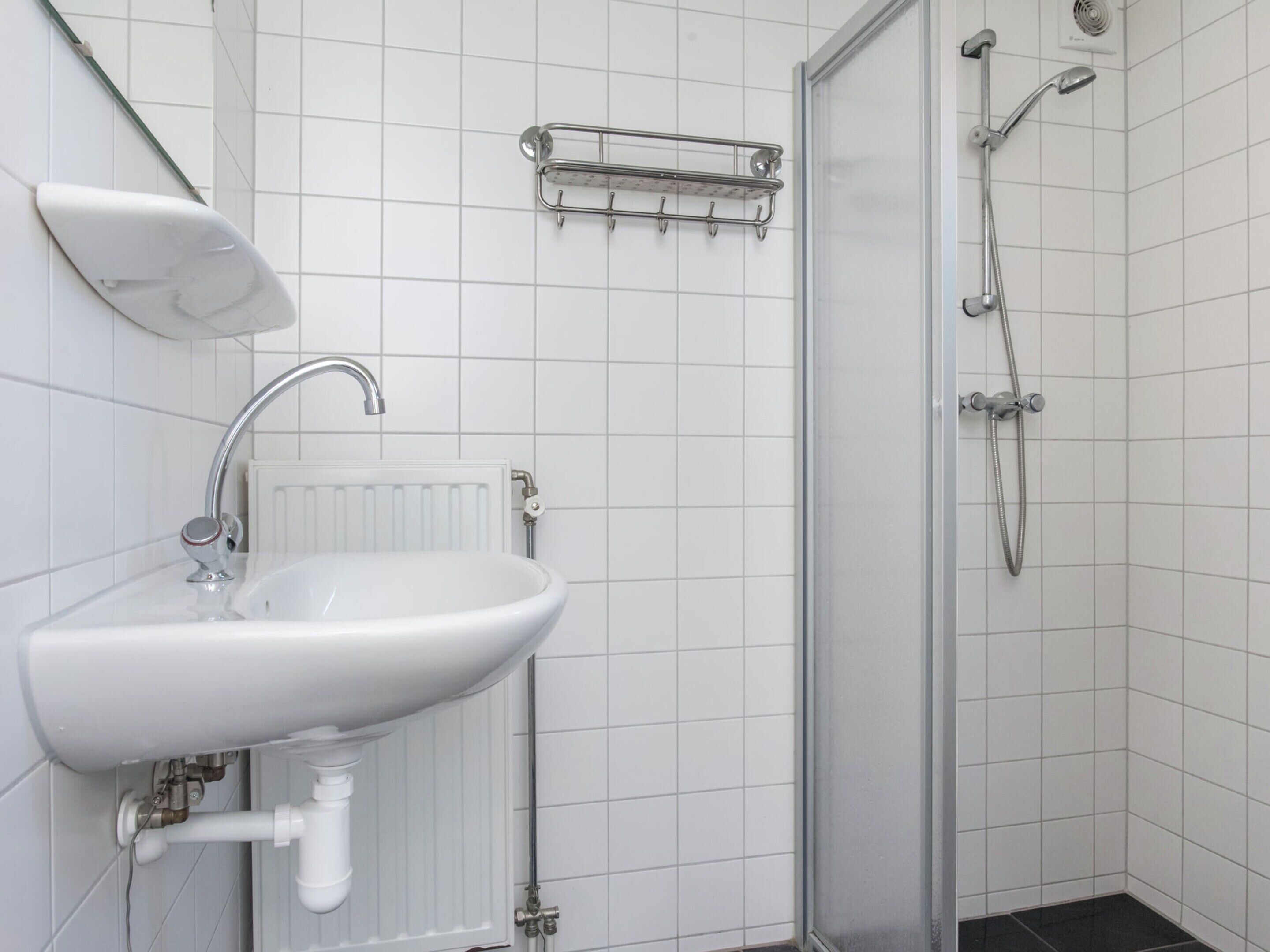 A bathroom with a white sink, a shower, and a towel rack.