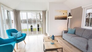 A modern living room with a large window, a grey sofa, a blue armchair, and a wooden coffee table. - Stylish Woodland Chalet (Hoge Hexel)