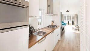 A modern kitchen with white cabinetry, a stainless steel stove, and a window overlooking a garden. - Stylish Woodland Chalet (Hoge Hexel)
