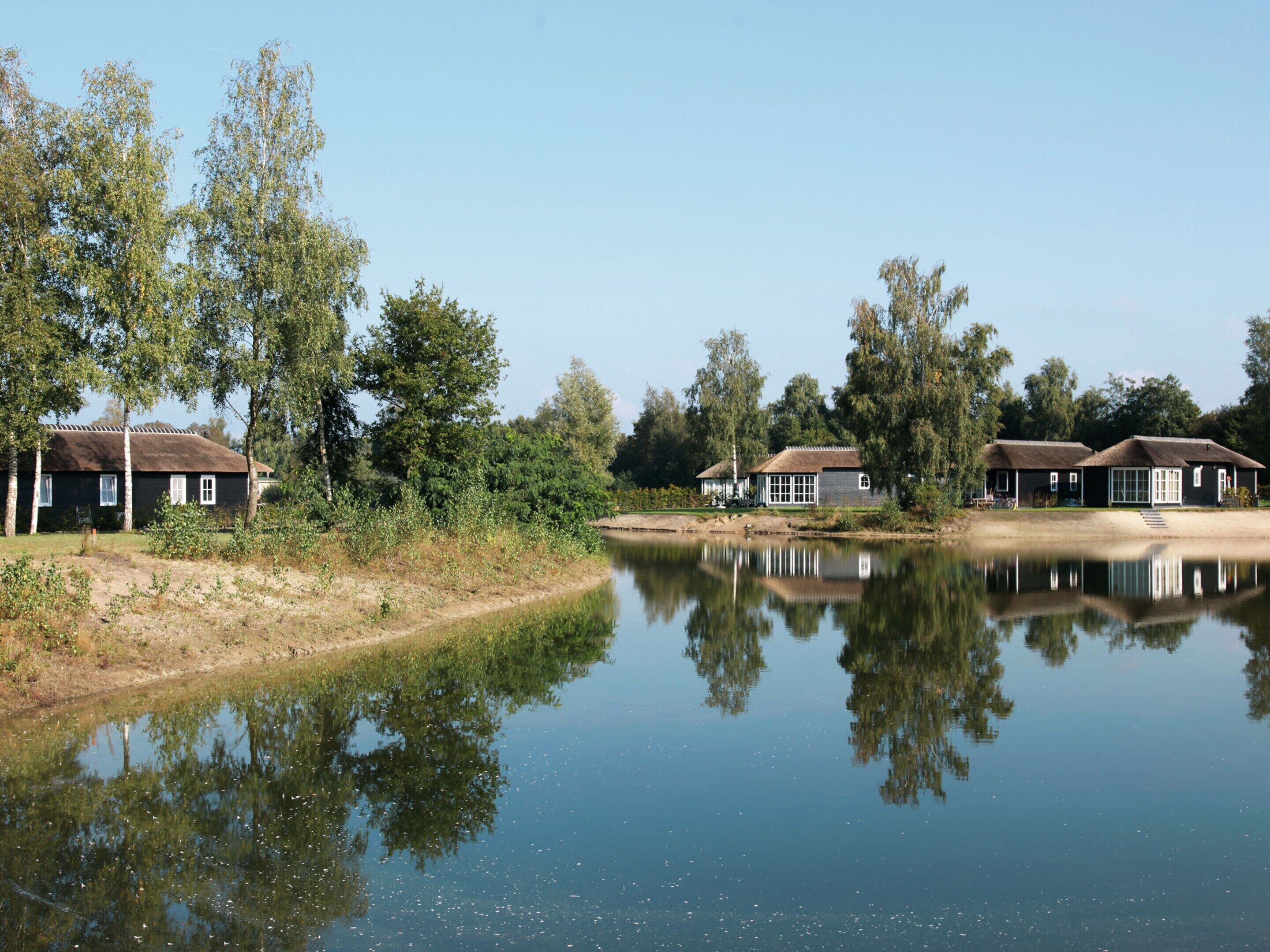 Een rustige oever met traditionele huisjes, een heldere weerspiegeling in het water en een natuurlijk landschap.
