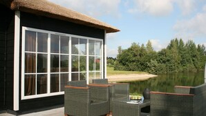 A house with a large glass window, outdoor wicker furniture, and a thatched roof. - Stylish Woodland Chalet (Hoge Hexel)