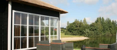 A house with a large glass window, outdoor wicker furniture, and a thatched roof.