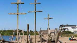 A wooden boat structure on a beach with a clear sky and a house in the background.
