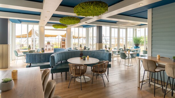 A spacious indoor area with high ceilings, large windows, and a mix of seating arrangements including sofas and tables.