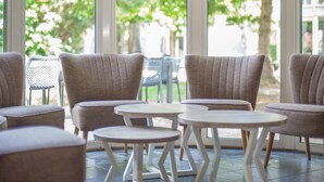 A seating area with cushioned chairs and small round tables, large windows with a view of greenery outside. - Restyled House with 5 Bathrooms near Vrachelse Heide (Oosterhout)