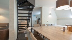A modern dining area with a wooden table and chairs, a staircase with black railings, and a white brick wall. - Restyled House with 5 Bathrooms near Vrachelse Heide (Oosterhout)