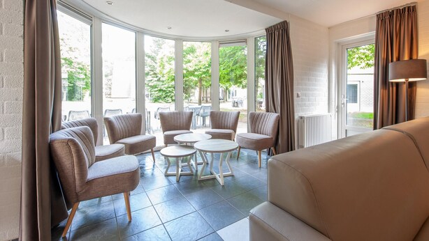 A modern lounge area with a curved glass wall, multiple seating options including sofas and round tables, and a large window providing a view of the outdoors. - Restyled House with 5 Bathrooms near Vrachelse Heide (Oosterhout)