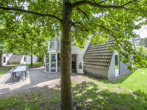 A modern house with a covered patio, a dining area, and a large tree providing shade. - Restyled House with 5 Bathrooms near Vrachelse Heide (Oosterhout)