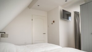 Un dormitorio con cama, puerta, televisor en la pared y armario.