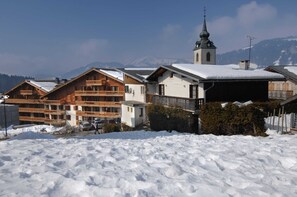 Ein verschneites Dorf mit Holzbauten, einer Kirche und Bergen im Hintergrund.