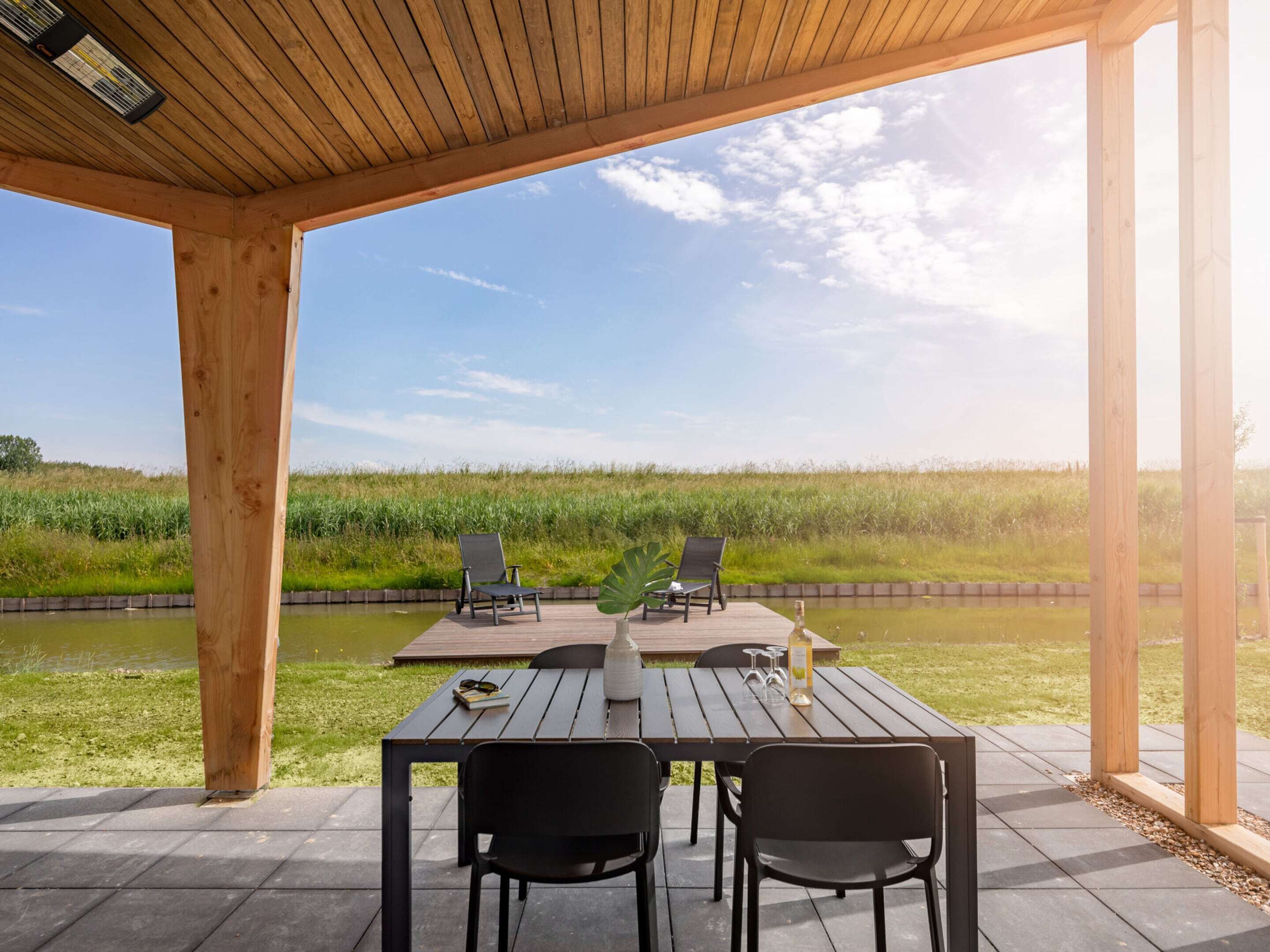 A wooden deck with a table and chairs overlooking a body of water and a grassy field.