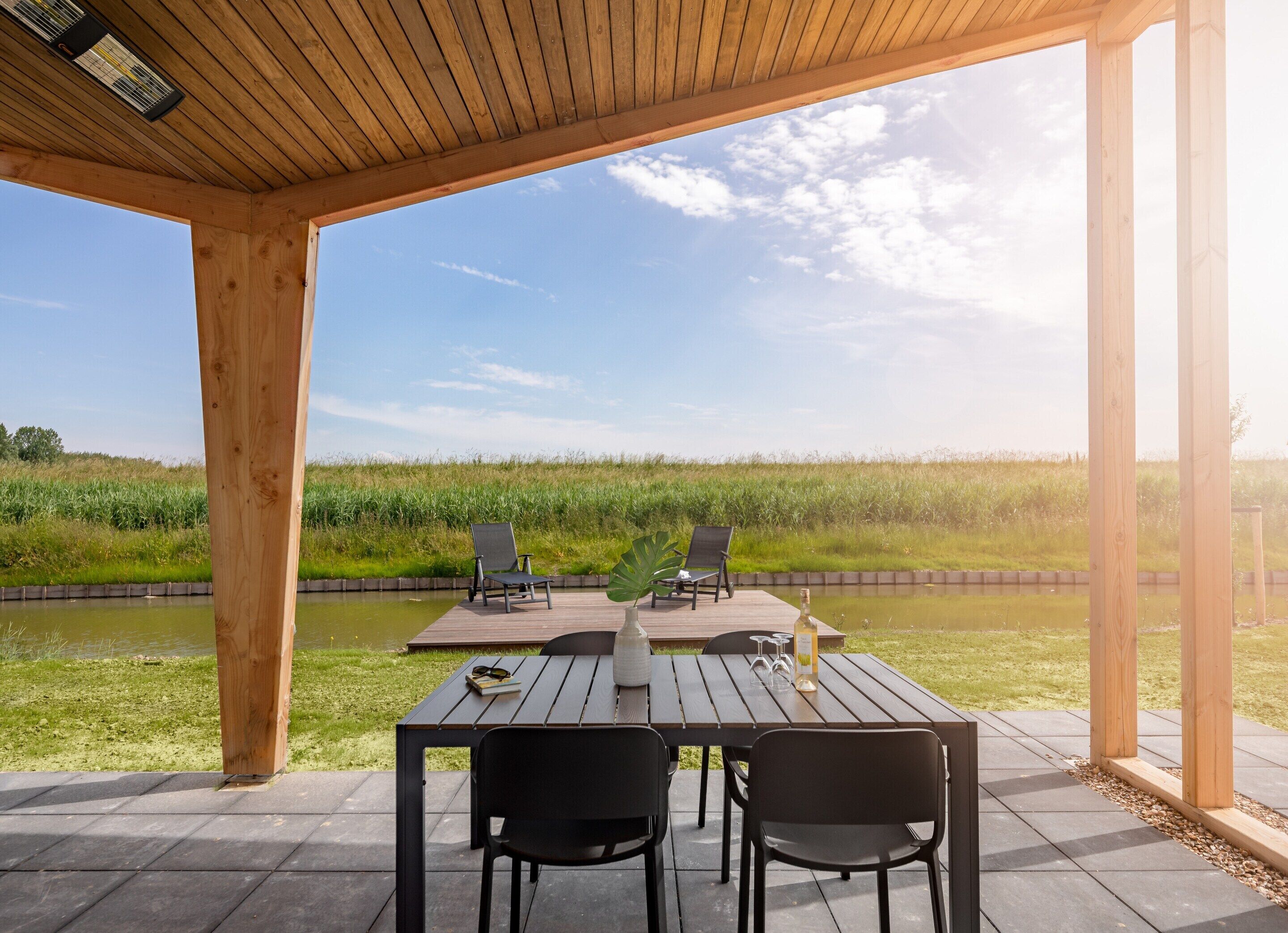 An outdoor wooden deck with a table and chairs, overlooking a grassy field and a body of water.