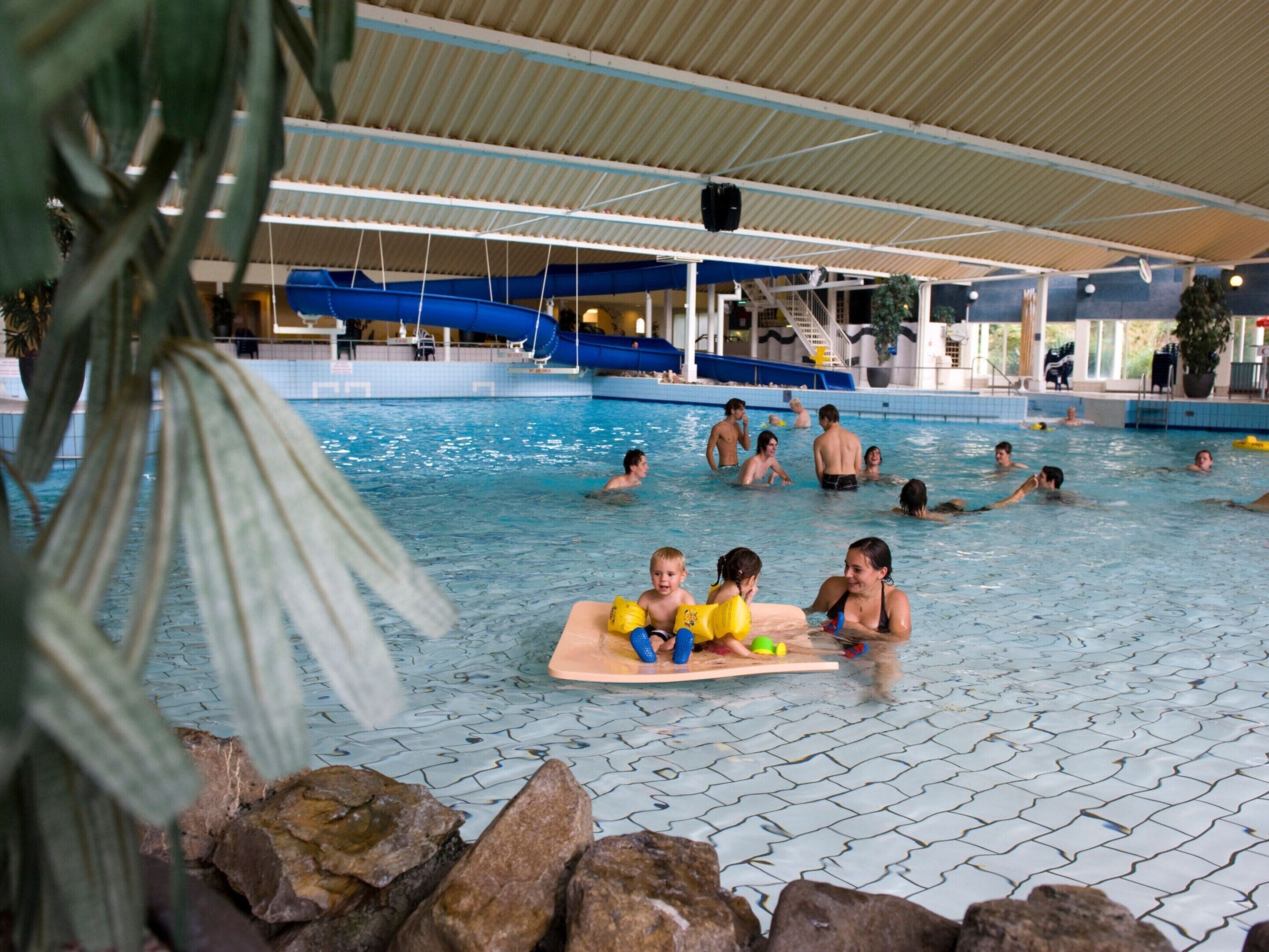 An indoor swimming pool with multiple lanes, a slide, and a covered seating area.