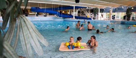 An indoor swimming pool with multiple lanes, a slide, and a covered seating area.