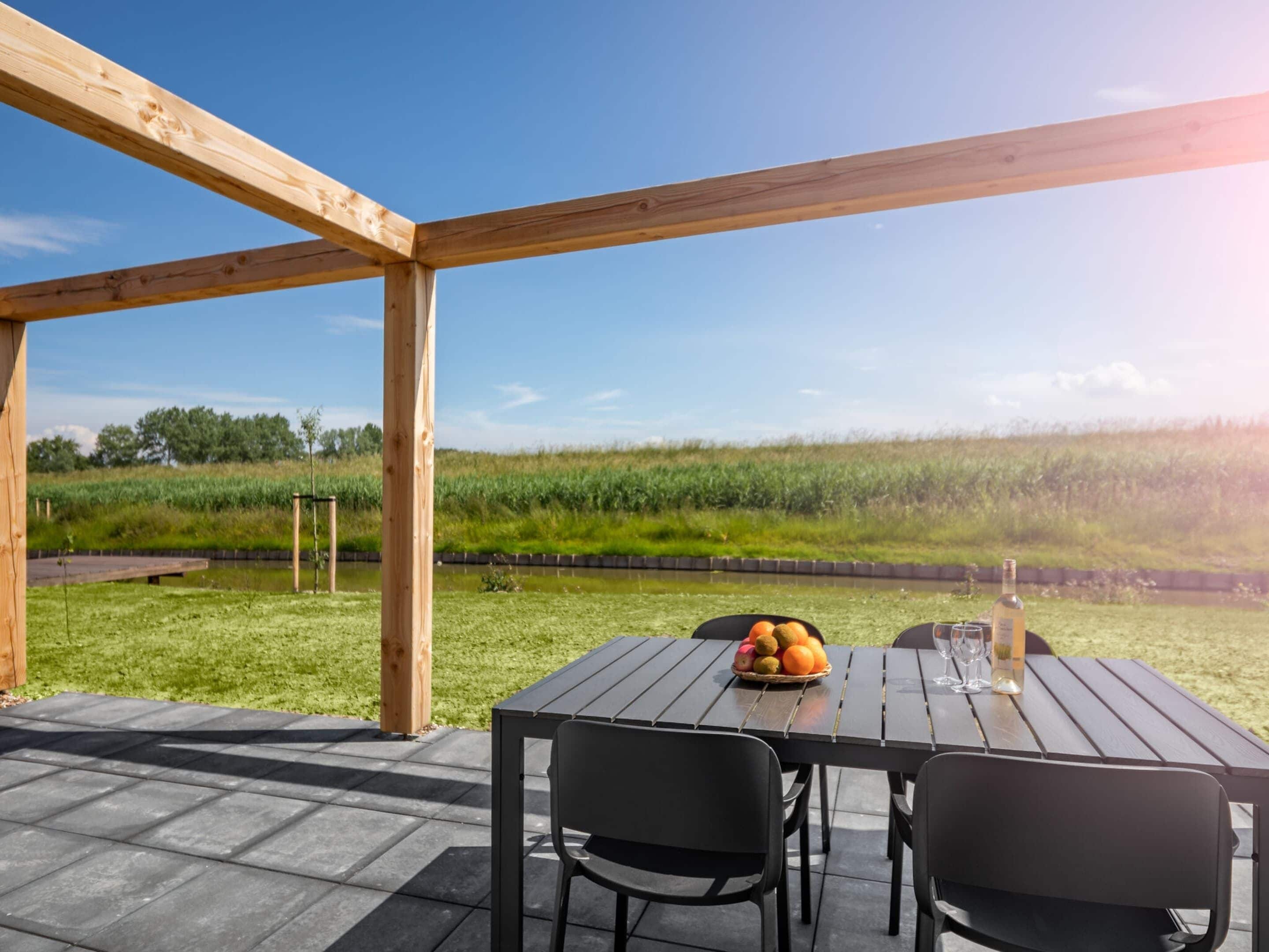 An outdoor wooden deck with a table and chairs, a basket of fruit, and a bottle of wine.