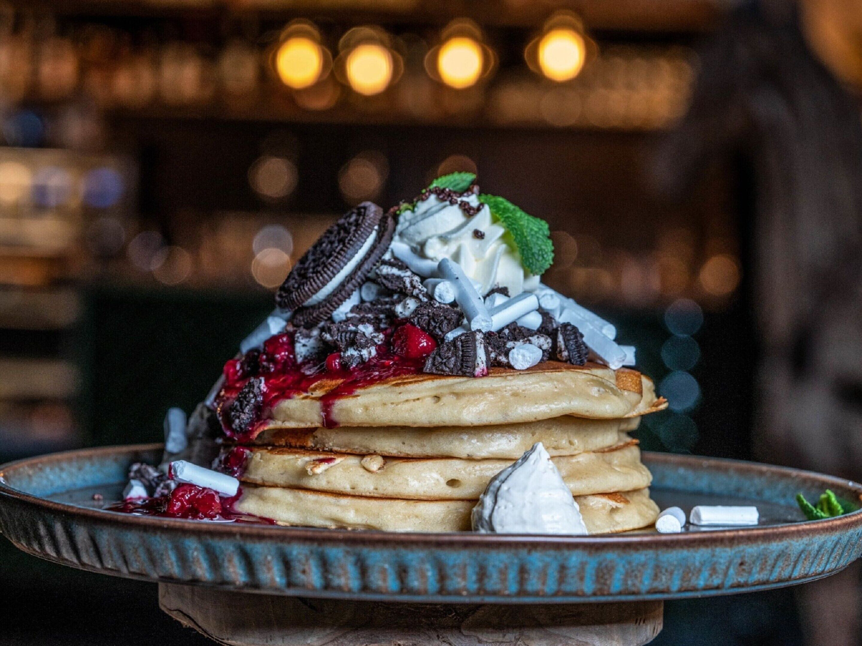 Une pile de crêpes garnie de crème fouettée, de fruits rouges et de pépites de chocolat.
